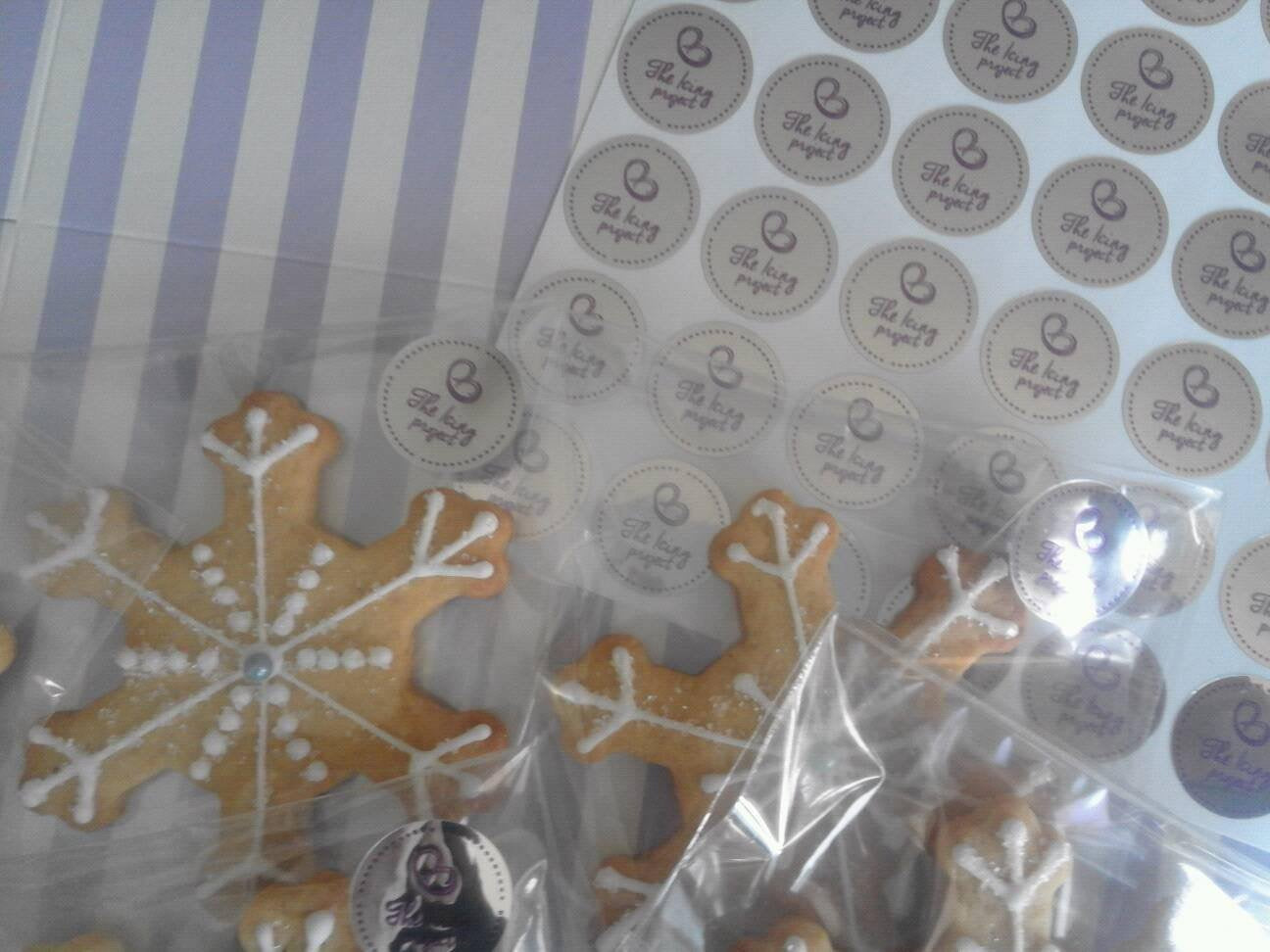Decorative cookies shaped like snowflakes with round The Icing Project labels in the background.