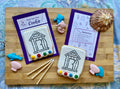 Decorative cookies with coloring sheets and paintbrushes on a wooden board.