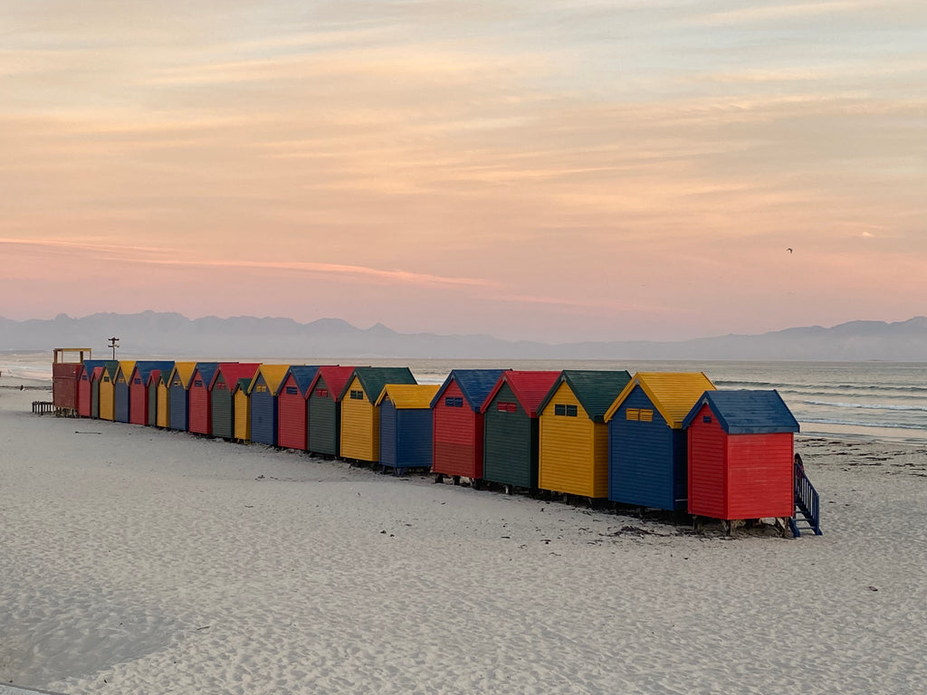 Row of colorful beach huts on a sandy beach with a pastel sky.